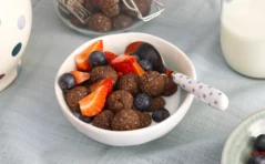 A white bowl full of chocolate balls and strawberries and blueberries