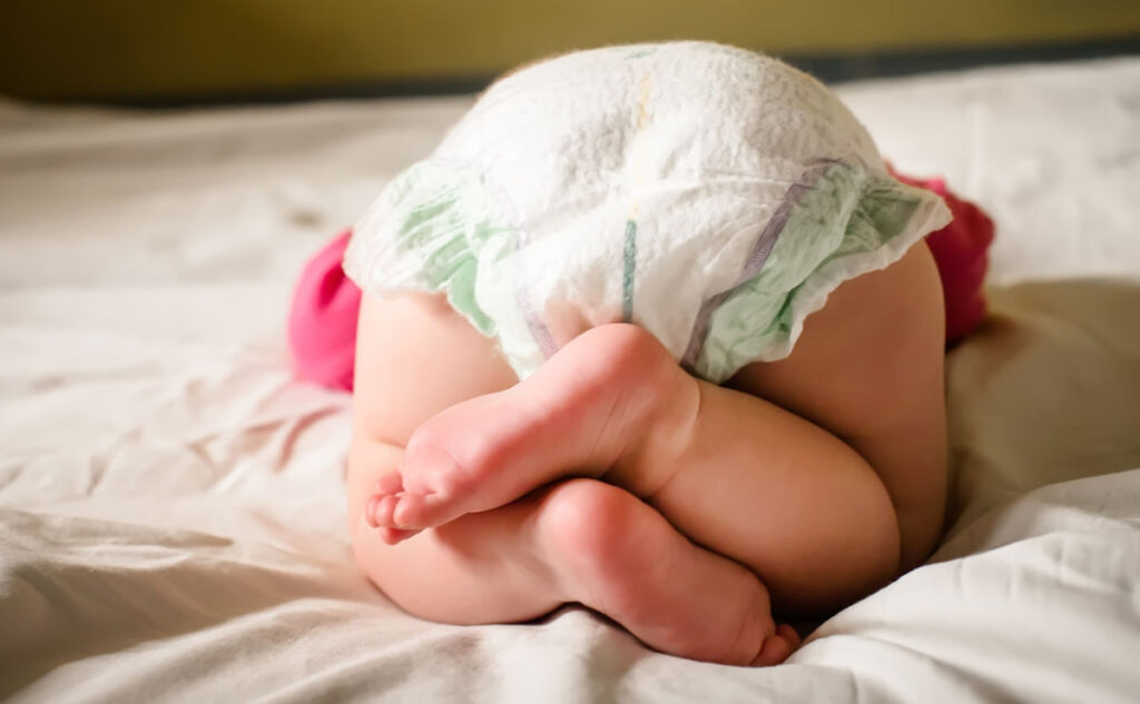 Baby wearing nappy lying on white bedding