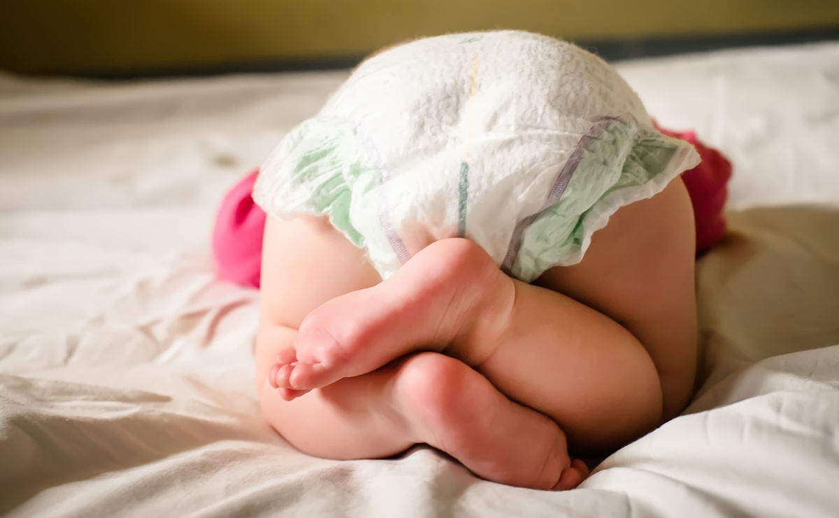Baby wearing nappy lying on white bedding