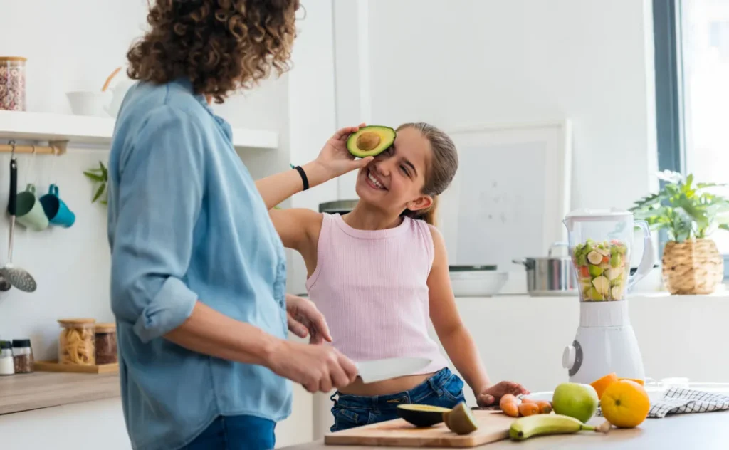 Mother and daughter cooking in the kitchen, chopping vegetables and fruit. Daughter is playing with avocado in kitchen.