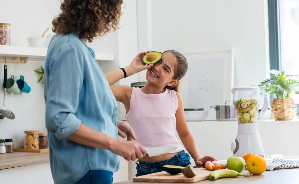 Mother and daughter cooking in the kitchen, chopping vegetables and fruit. Daughter is playing with avocado in kitchen.