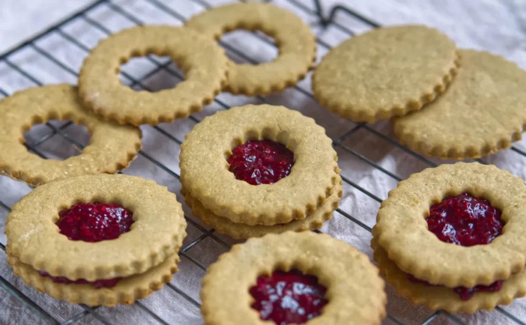 Golden biscuits with jam peeping through a hole at the top -cooling on a wire rack.