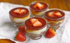4 glass bowls full of custard and strawberry and rhubarb Compote, two slices of strawberry are on top of each one.