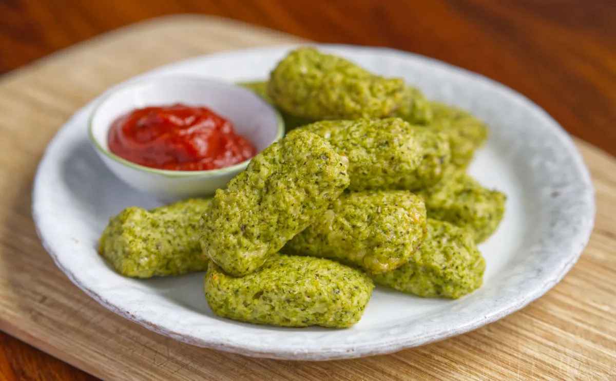 white plate full of broccoli croquettes with a small bowl of ketchup on the side
