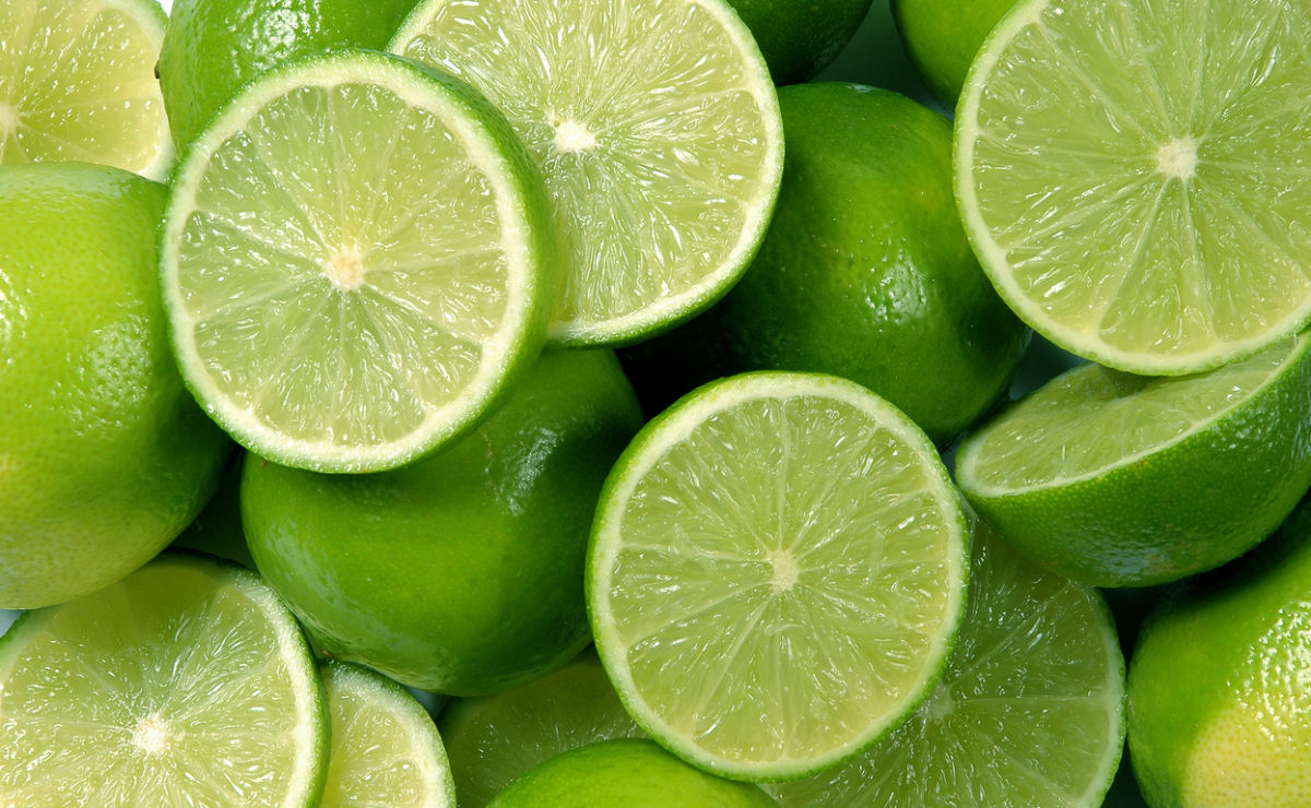 A close-up of several fresh green limes, some whole and some sliced in half, showing their juicy interior and vibrant color.