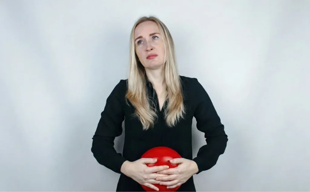 Blonde woman in black top holding red hot water bottle