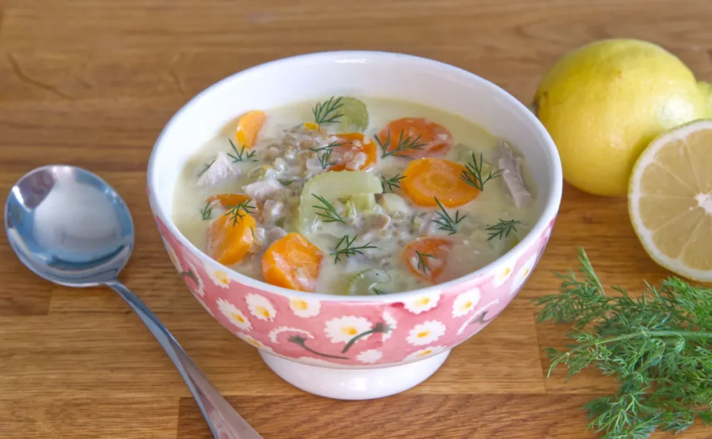 A bowl of soup with vegetables and a lemon.