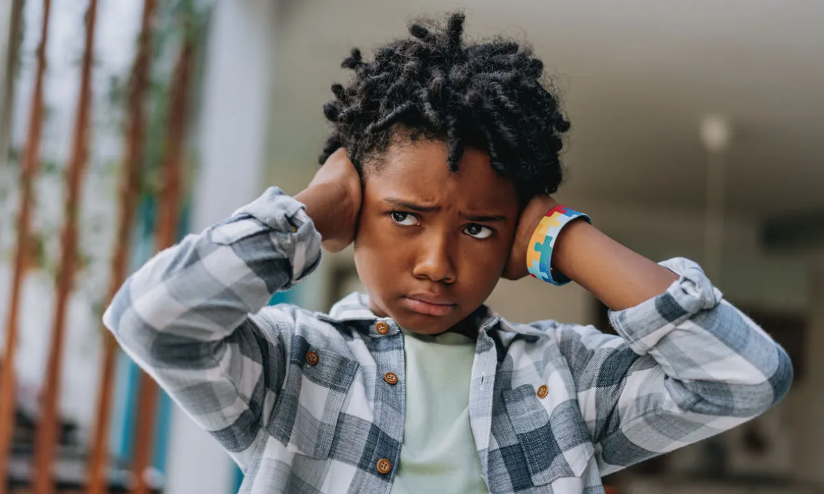 Young boy in checked shirt covering his ears.