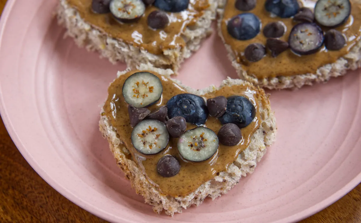 Peanut butter spread on heart shaped slices of bread topped with blueberries and chocolate chips