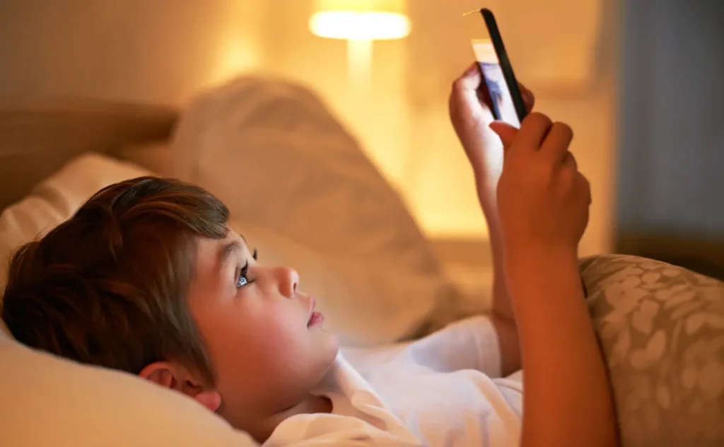 Boy using smartphone in bed with warm lighting