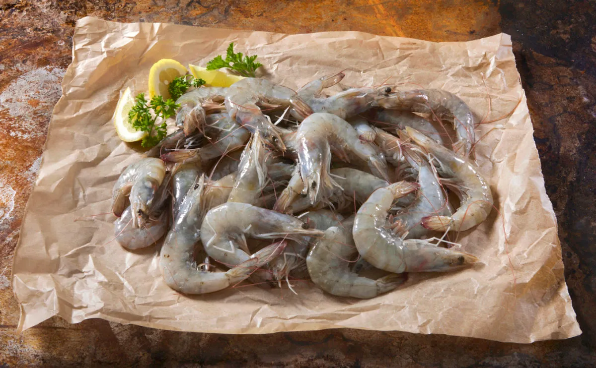 Raw Prawns on baking paper on top of a wooden board with lemon and parsley as a garnish