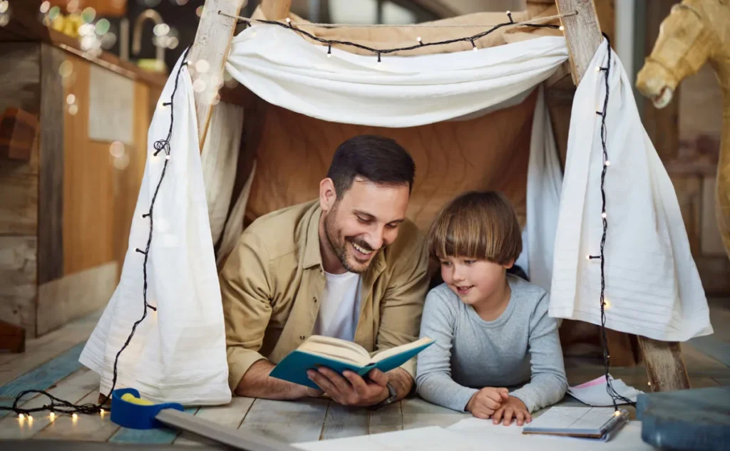 A father and son reading happily together in a home made den.