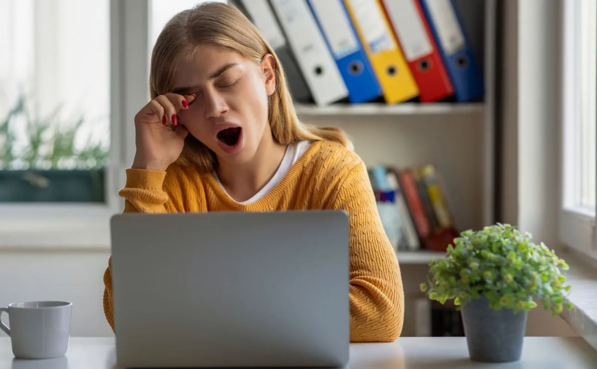 Tired young woman yawning at laptop in office