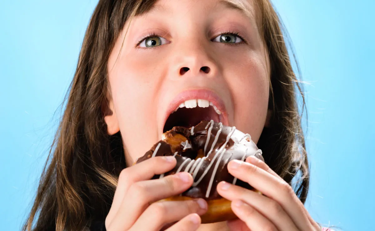 Girl eating chocolate doughnut with white drizzle