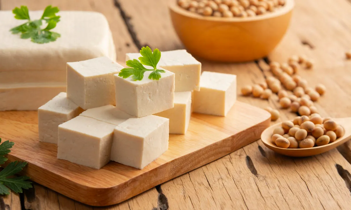 Cubes of tofu on a board, with soya beans next to it in another bowl, scattered with herbs.