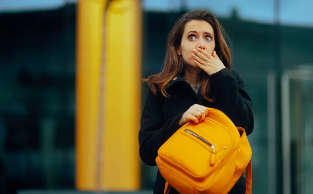 Women realising she has forgotten something - holding a yellow backpack, she covers her mouth shocked, with her other hand