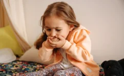 Little girl in apricot coloured dressing gown, holding her hands over her mouth as if she is about to be sick