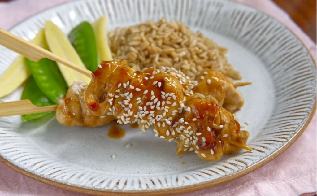 chicken skewers on a white plate, sprinkled with sesame seeds