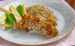 chicken skewers on a white plate, sprinkled with sesame seeds