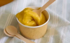 A brown tub lying on a blue and white tea towel full of soft orange sorbet. Small wooden spoons scattered alongside it.