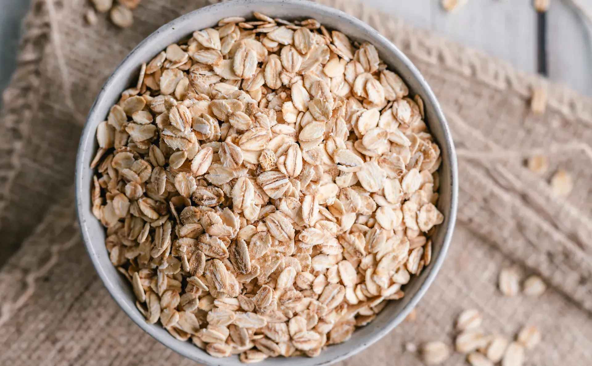 A bowl of oats on hessian sacking with a few oats strewn around.